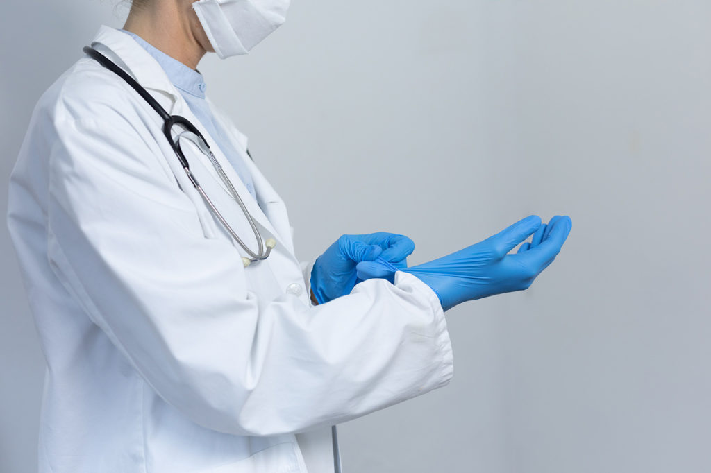 Mid section of a Caucasian female healthcare worker wearing a lab coat and face mask against coronavirus, covid 19, putting on surgical gloves.